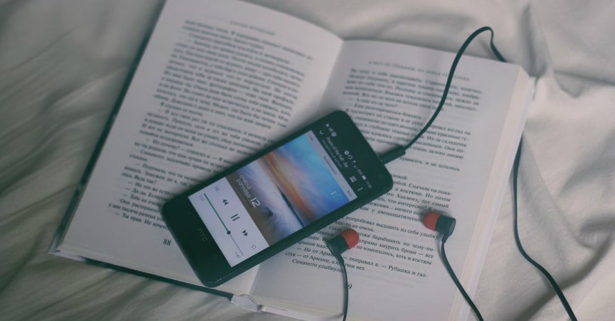 smartphone with earbuds and the book lying on the bed